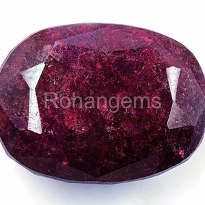 May include: A deep red oval gemstone with a faceted cut. The gemstone has a slightly cloudy appearance with a few visible inclusions.