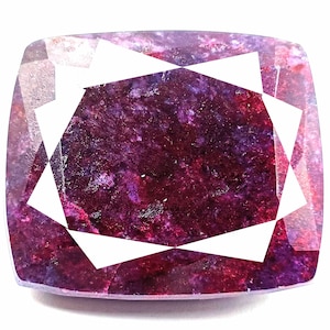 Puede incluir: Una piedra preciosa de color rojo intenso con un corte facetado y un patrón de estrella. La piedra preciosa tiene un tono púrpura y una apariencia nublada.