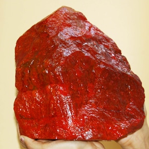 May include: A large, irregularly shaped, red gemstone. The gemstone has a smooth, polished surface and is a deep, rich red color.