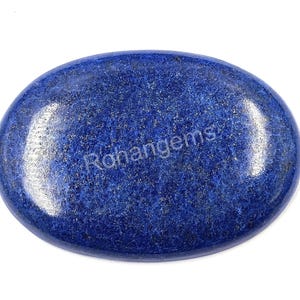 Pode incluir: Gema ovalada de lápis-lazúli polido. A pedra azul escura tem uma textura salpicada e um acabamento brilhante. A palavra "Rohangems" é visível na superfície. Esta gema é adequada para a fabricação de joias.