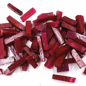 May include: A pile of small, rectangular ruby red gemstone pieces. The pieces are all roughly the same size and shape, and they are arranged in a random pattern.