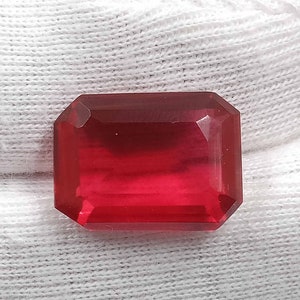 May include: A deep red gemstone with a rectangular emerald cut.