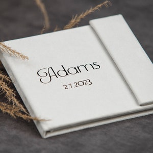 May include: White photo album with the name "Adams" and the date "2.7.2023" printed on the front.