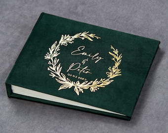 May include: A dark green velvet photo album with a gold foil design. The design features a wreath of leaves and the text "Emily & Peter 03 03 2023".