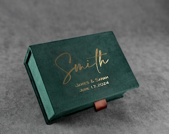 May include: A green velvet box with a gold inscription that reads "Smith, James & Sarah, June 17, 2024".