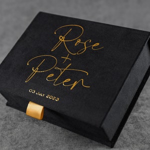 Può includere: Scatola in velluto nero con scritta dorata "Rose + Peter" e "03 luglio 2023".