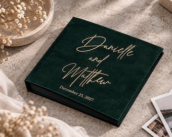 May include: A square dark green velvet photo album featuring gold foil lettering that reads Danielle and Matthew with the date December 25, 2027, printed in a smaller font underneath the names on the front cover.