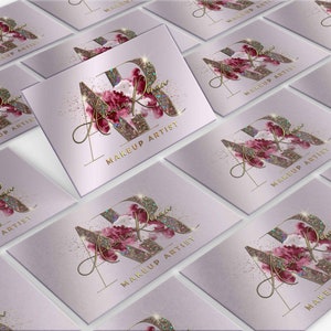 Op de afbeelding: Een verzameling visitekaartjes met een lichtpaarse achtergrond. Elk kaartje heeft een goudkleurig "AR" monogram met een bloemenontwerp en de woorden "MAKEUP ARTIST" in goud. Het ontwerp bevat glitteraccenten.