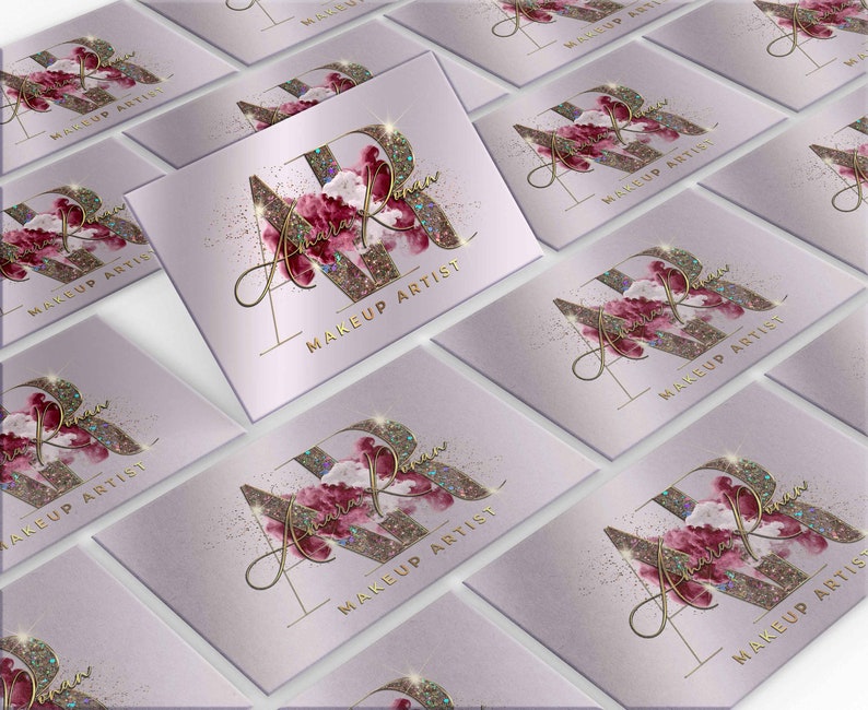 Op de afbeelding: Een verzameling visitekaartjes met een lichtpaarse achtergrond. Elk kaartje heeft een goudkleurig "AR" monogram met een bloemenontwerp en de woorden "MAKEUP ARTIST" in goud. Het ontwerp bevat glitteraccenten.