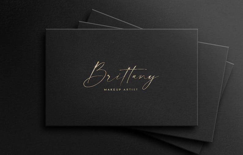 May include: A black business card with gold lettering that reads "Brittany Makeup Artist".