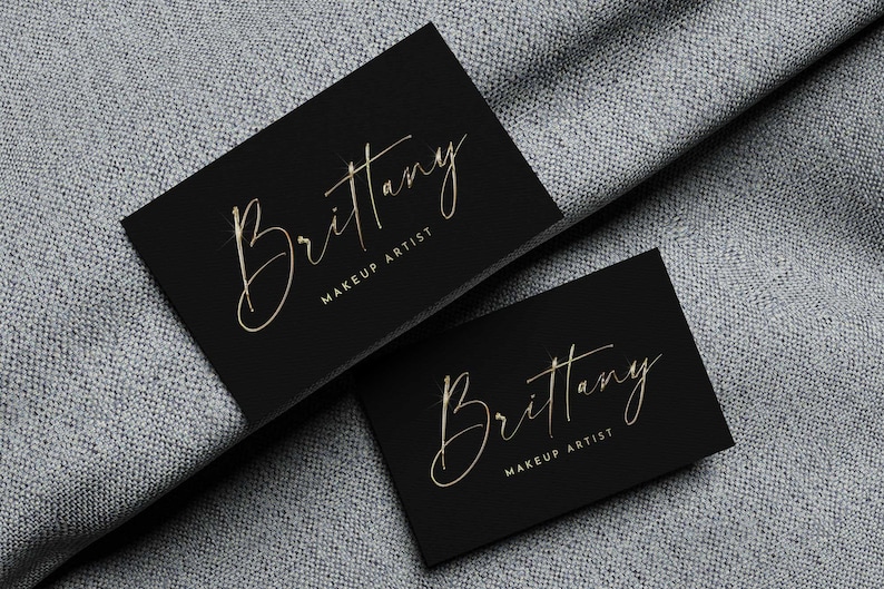 May include: Two black business cards with gold lettering. The text on the cards reads "Brittany Makeup Artist".