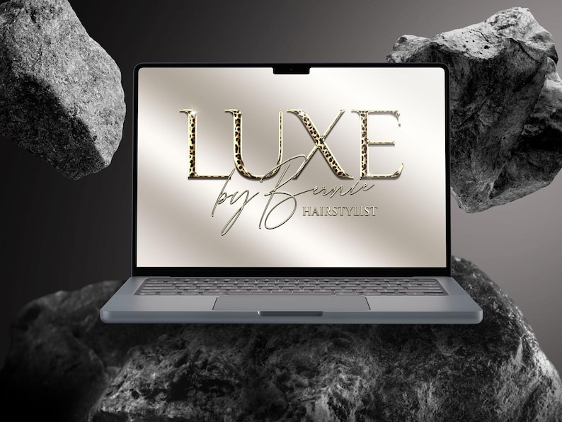 May include: A laptop computer displays the text "LUXE by Denise HAIRSTYLIST" on its screen. The word "LUXE" features a leopard print pattern. The laptop is gray and rests on a dark, textured surface, with large rocks in the background.