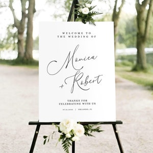 May include: White wedding welcome sign with black calligraphy text that reads "Welcome to the wedding of Monica + Robert" and "Thanks for celebrating with us 07.16.2030 Orlando, FL".