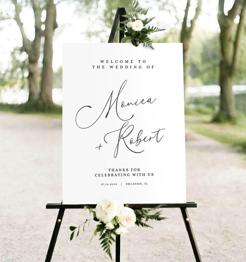 May include: White wedding welcome sign with black calligraphy text that reads "Welcome to the wedding of Monica + Robert" and "Thanks for celebrating with us 07.16.2030 Orlando, FL".