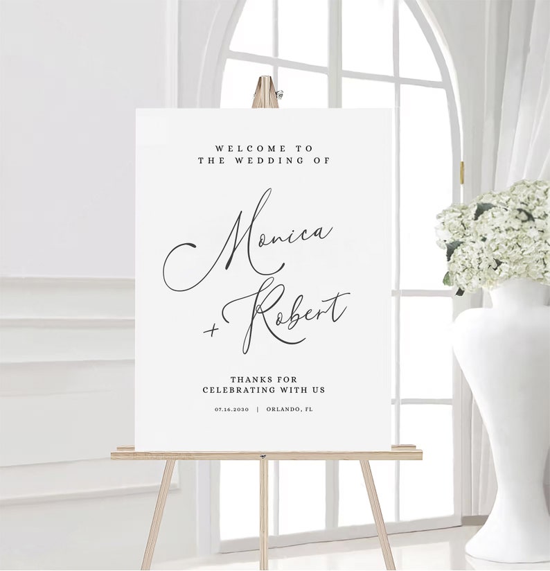 May include: White wedding welcome sign with black text. The sign reads "Welcome to the wedding of Monica + Robert. Thanks for celebrating with us. 07.16.2030 Orlando, FL"