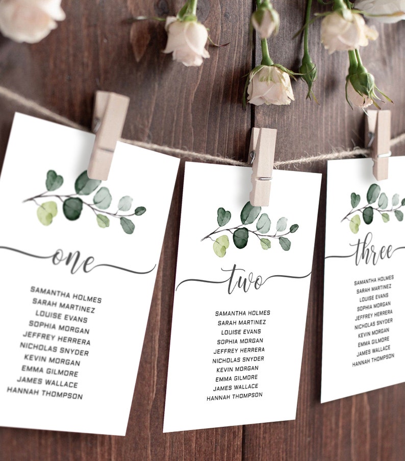 May include: Three white cards with green watercolour leaves and the words "one", "two", and "three" written in black calligraphy. Each card lists a set of names for a wedding seating chart.