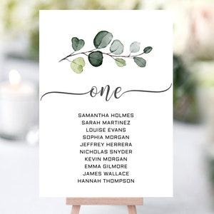 May include: A white card with a watercolour illustration of a eucalyptus branch with green leaves. The card has the word "one" written in cursive and a list of names below it.