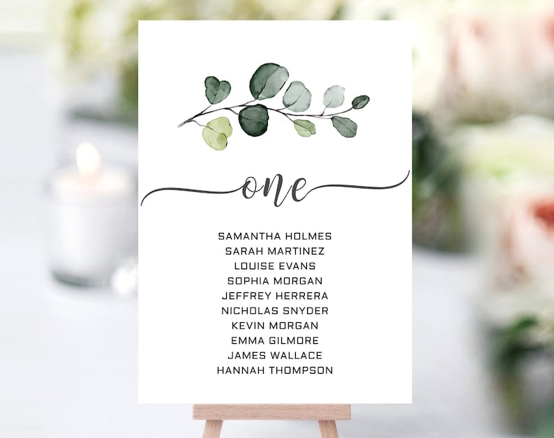May include: A white card with a watercolour illustration of a eucalyptus branch with green leaves. The card has the word "one" written in cursive and a list of names below it.