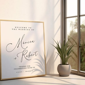 May include: A framed wedding sign with a white background and black text. The sign reads "Welcome to the wedding of Monica + Robert. Thanks for celebrating with us. 03.16.2019 | Orlando, FL."