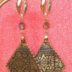 May include: A pair of gold-tone earrings with a diamond-shaped fabric design and a shell charm. The fabric is a dark green with gold accents.