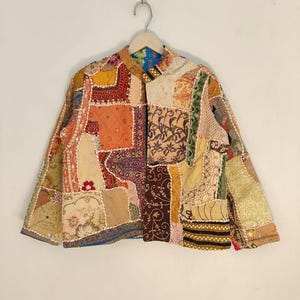 May include: A patchwork jacket with a mandarin collar, featuring a variety of fabric patterns and colors. The jacket is made of different fabric squares in shades of orange, yellow, brown, and cream, with floral and geometric designs.