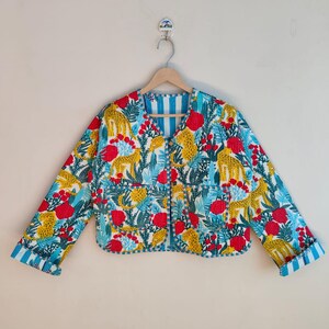May include: A patterned jacket with a striking design. The jacket features a blue, red, and yellow floral and animal print. The jacket is hanging on a wooden hanger against a white wall.