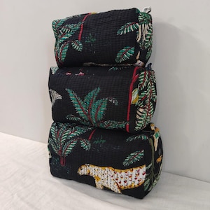 May include: Three black cylindrical bags stacked on top of each other. Each bag features a vibrant tropical print with green palm leaves, red accents, and a white and yellow leopard. The bags are made of a quilted fabric.
