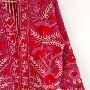 May include: A magenta jacket with floral embroidery in shades of red and pink. The jacket features a mandarin collar and long sleeves. The interior lining is striped. The embroidery includes flowers and leaf patterns.