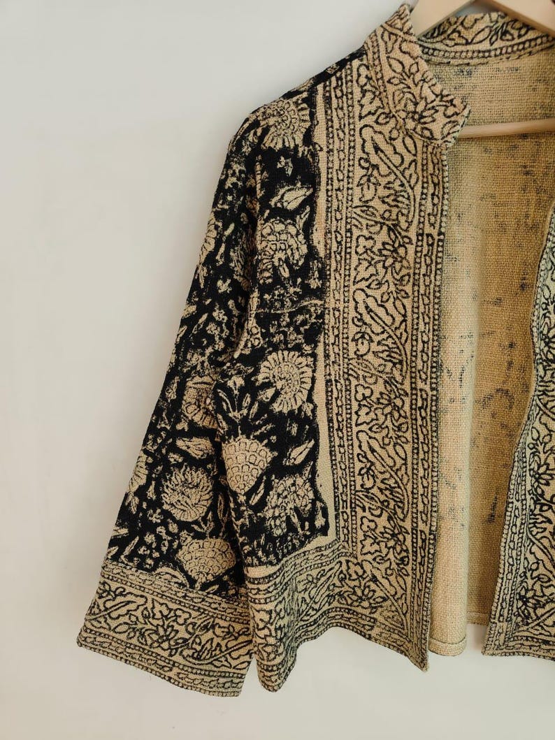 K&ouml;nnte beinhalten: Beige und schwarze Jacke mit floralem und geometrischem Muster. Die Jacke hat einen Stehkragen und Dreiviertel&auml;rmel. Der Stoff scheint ein gewebtes Material zu sein.