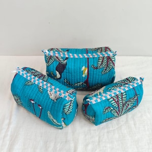 Può includere: Tre trousse per cosmetici turchesi con stampa tropicale con tucani e palme. Le borse hanno una texture trapuntata e un bordo a righe bianche e rosse lungo la cerniera.