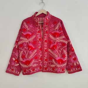 May include: A magenta jacket with intricate floral embroidery in shades of red and pink. The jacket features a mandarin collar and long sleeves. The embroidery includes flowers and leaf patterns, creating a detailed design.
