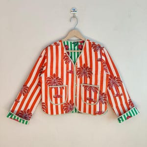 May include: A reversible jacket with a striped pattern in red and white, featuring palm tree designs. The jacket has two pockets and green trim. The inside lining is green with a floral pattern.
