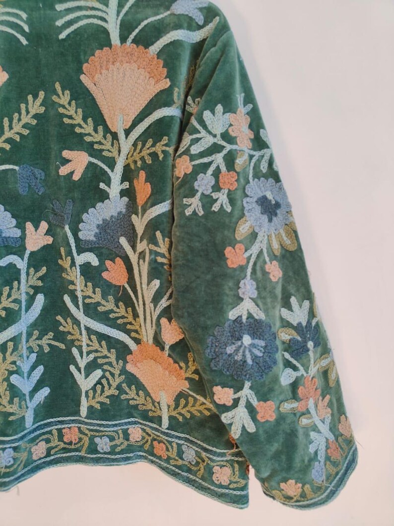 Puede incluir: Chaqueta de terciopelo verde con intrincado bordado floral en tonos melocot&oacute;n, azul y crema. El bordado cubre las mangas y el frente, con un borde detallado en el dobladillo. El dise&ntilde;o de la chaqueta presenta un tema bot&aacute;nico.