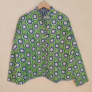 May include: A green jacket featuring a blue and white floral design. The jacket has a collared neckline and long sleeves. The interior lining is striped blue and white. The jacket is hanging on a wooden hanger.