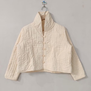 May include: A cream-coloured quilted jacket with a high collar and button closure. The jacket features a boxy silhouette and a subtle quilted pattern. The neutral colour and simple design make it a versatile outerwear piece.