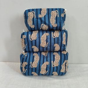 Può includere: Tre contenitori rettangolari impilati. Ogni contenitore è blu scuro con strisce verticali e un motivo ripetuto di stampa leopardata beige. I contenitori sono realizzati in tessuto trapuntato e hanno finiture bianche.