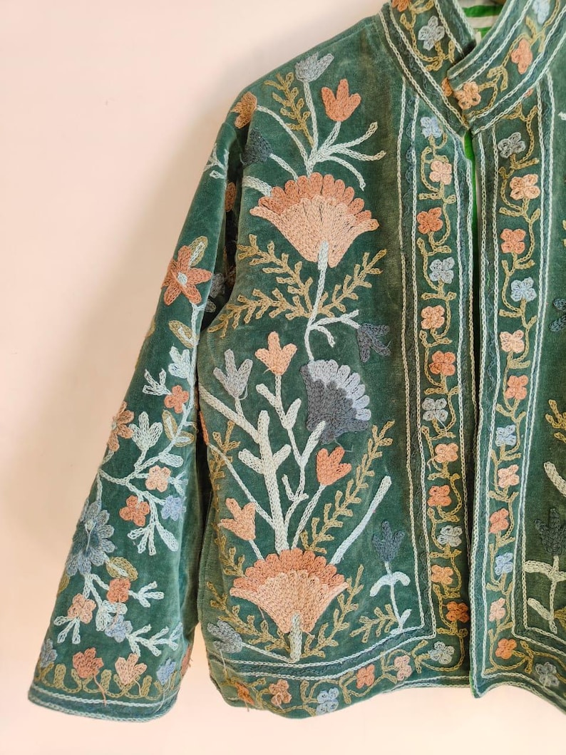 Puede incluir: Chaqueta de terciopelo verde con intrincados bordados florales en tonos melocot&oacute;n, azul y crema. La chaqueta presenta un cuello mandar&iacute;n y bordados detallados en las mangas y bordes delanteros, de estilo bohemio.
