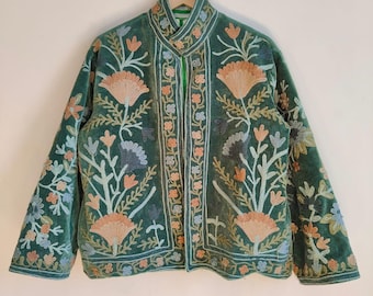 May include: A green velvet jacket with intricate floral embroidery in shades of peach, blue, and white. The jacket features a mandarin collar and is hanging on a wooden hanger. The embroidery covers the front, sleeves, and collar.
