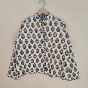 May include: A white jacket featuring a blue floral pattern and a blue striped lining. The jacket is buttoned and suspended from a wooden hanger. The floral design is repeated across the garment.