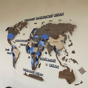 May include: A wooden world map in shades of brown, blue, and beige is displayed on a wall. The oceans are labelled in black text. A compass rose is in the lower right corner. The map is a decorative item.