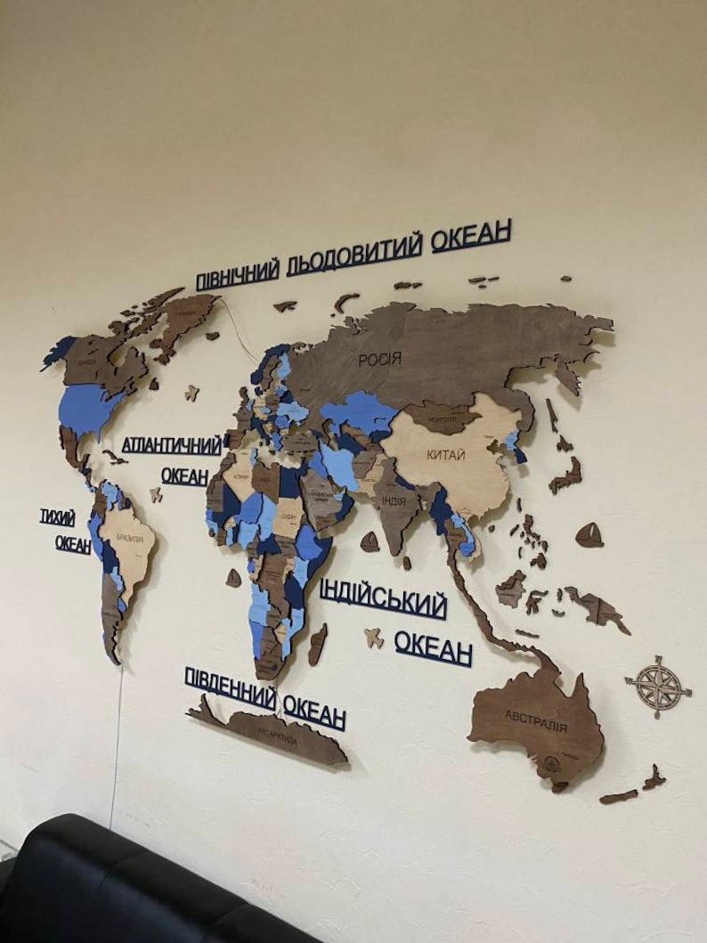 May include: A wooden world map in shades of brown, blue, and beige is displayed on a wall. The oceans are labelled in black text. A compass rose is in the lower right corner. The map is a decorative item.