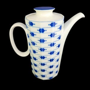 May include: White ceramic coffee pot with a blue floral pattern and a matching lid. The pot has a curved handle and a long spout. The design features blue floral motifs and dots on a white background. The lid is topped with a blue knob.