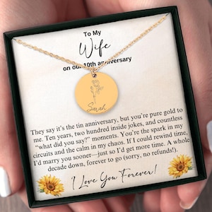 May include: A gold-colored necklace with a round pendant featuring a rose design and the name "Sarah." The necklace is presented in a black box with text that reads "To My Wife on our 10th anniversary" and "I Love You Forever!"