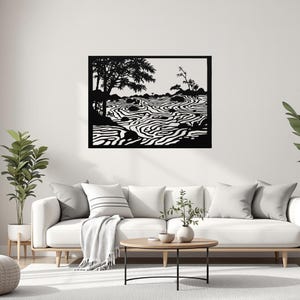 May include: Black metal wall art depicting a serene landscape with a river, trees, and rocks. The artwork is a silhouette, with the details cut out to create a contrast against the background. The piece is mounted on a white wall above a white sofa.