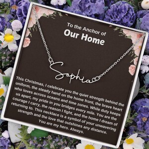 May include: A silver necklace with the name "Sophia" in cursive script. The necklace is presented on a card with the text "To the Anchor of Our Home" and a message about love and strength. The background features floral accents.