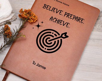 Könnte beinhalten: Ein braunes Lederjournal mit den Worten "BELIEVE. PREPARE. ACHIEVE." und einer Zielscheibengrafik. Das Journal ist personalisiert mit "From Mrs. Bonnie Aarons" und "To Jamie."