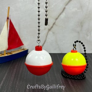 May include: Two red and white fishing bobbers with black and silver chains. The bobbers are hanging from the ceiling. The bobbers are a popular choice for fishing enthusiasts.