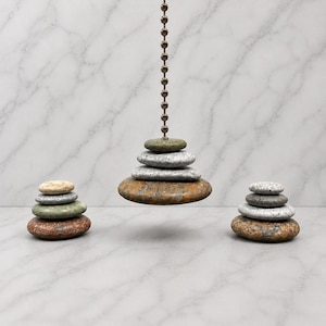 May include: A ceiling fan pull chain featuring a stack of four smooth, rounded stones in shades of green, gray, and brown. Two additional stacks of four stones each are positioned on either side, mirroring the colors and shapes of the central piece.