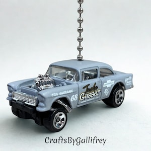 May include: A light blue die-cast model car with a chrome engine and wheels. The car has the text "Turbo Gasser 68" and "Chevrolet" on the side. A silver chain is attached to the top of the car.