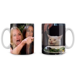May include: A white ceramic mug with a black handle. The mug features two images. One side shows a woman yelling at the camera with her finger pointed. The other side shows a white cat with a confused expression looking at a plate of food.